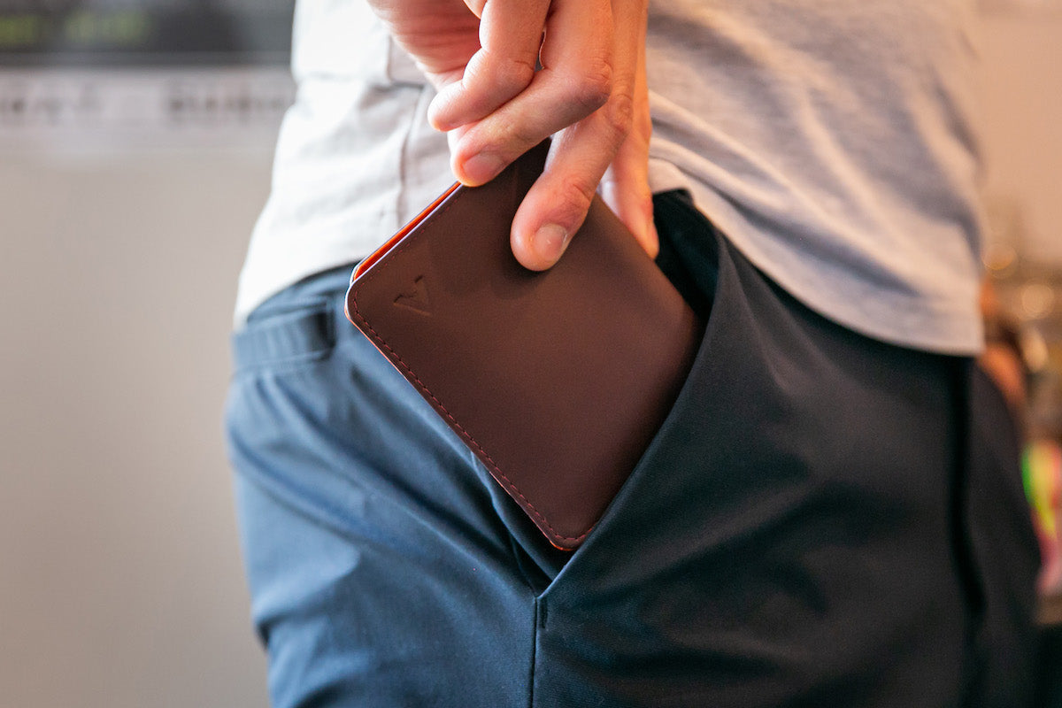 Man putting a thin brown leather wallet into his front pocket.