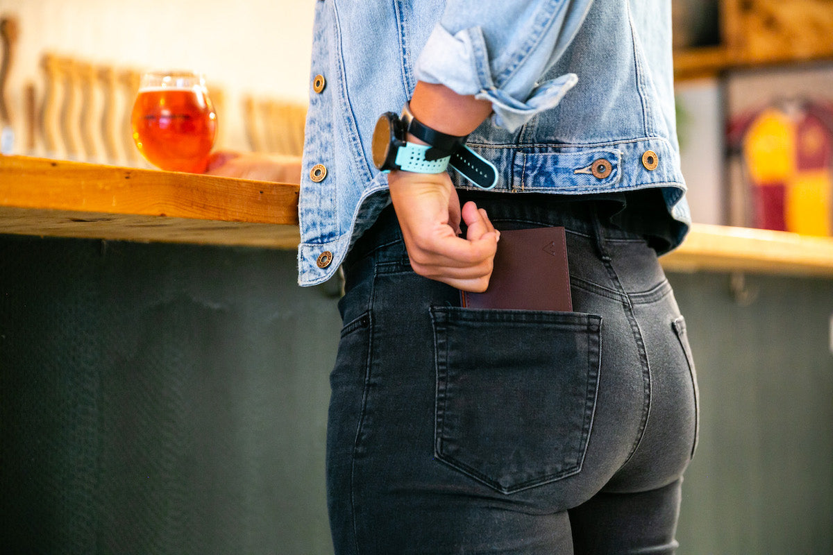 Young woman wearing tight black jeans takes a thin leather wallet from her back pocket.