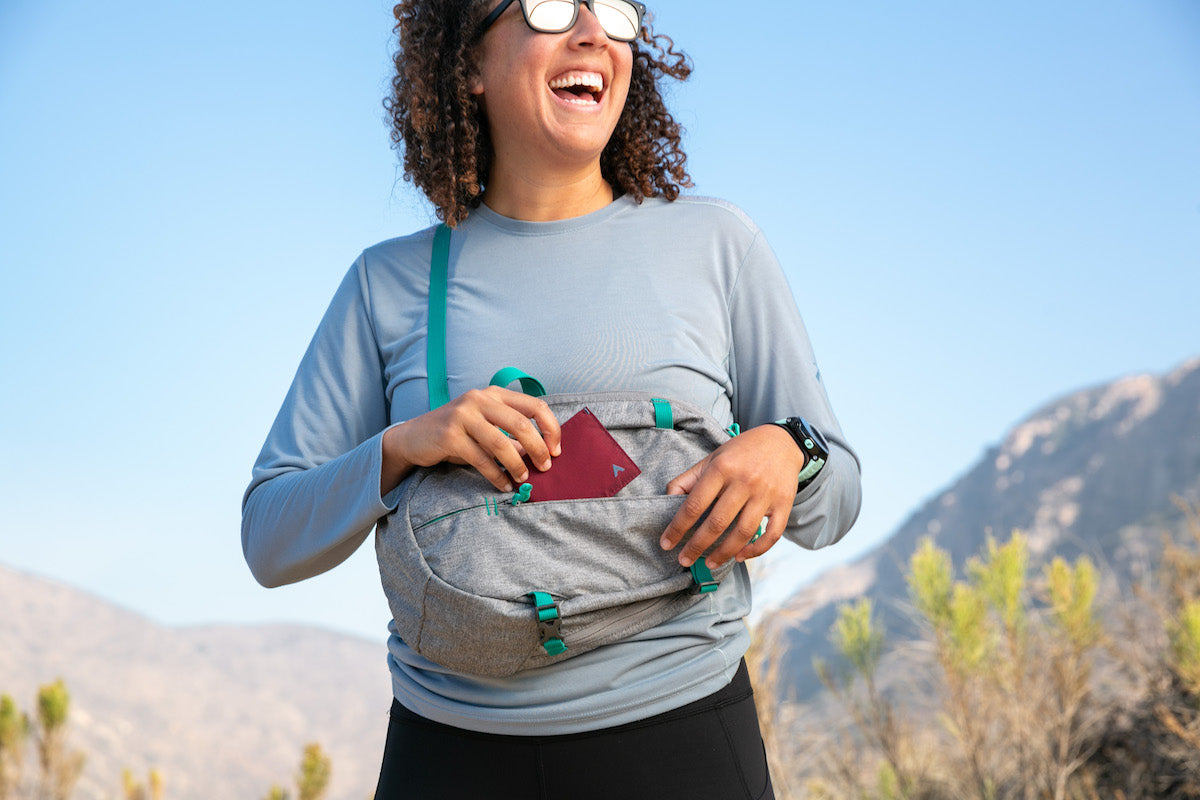 Happy woman putting a thin maroon women's wallet into a light grey bag.