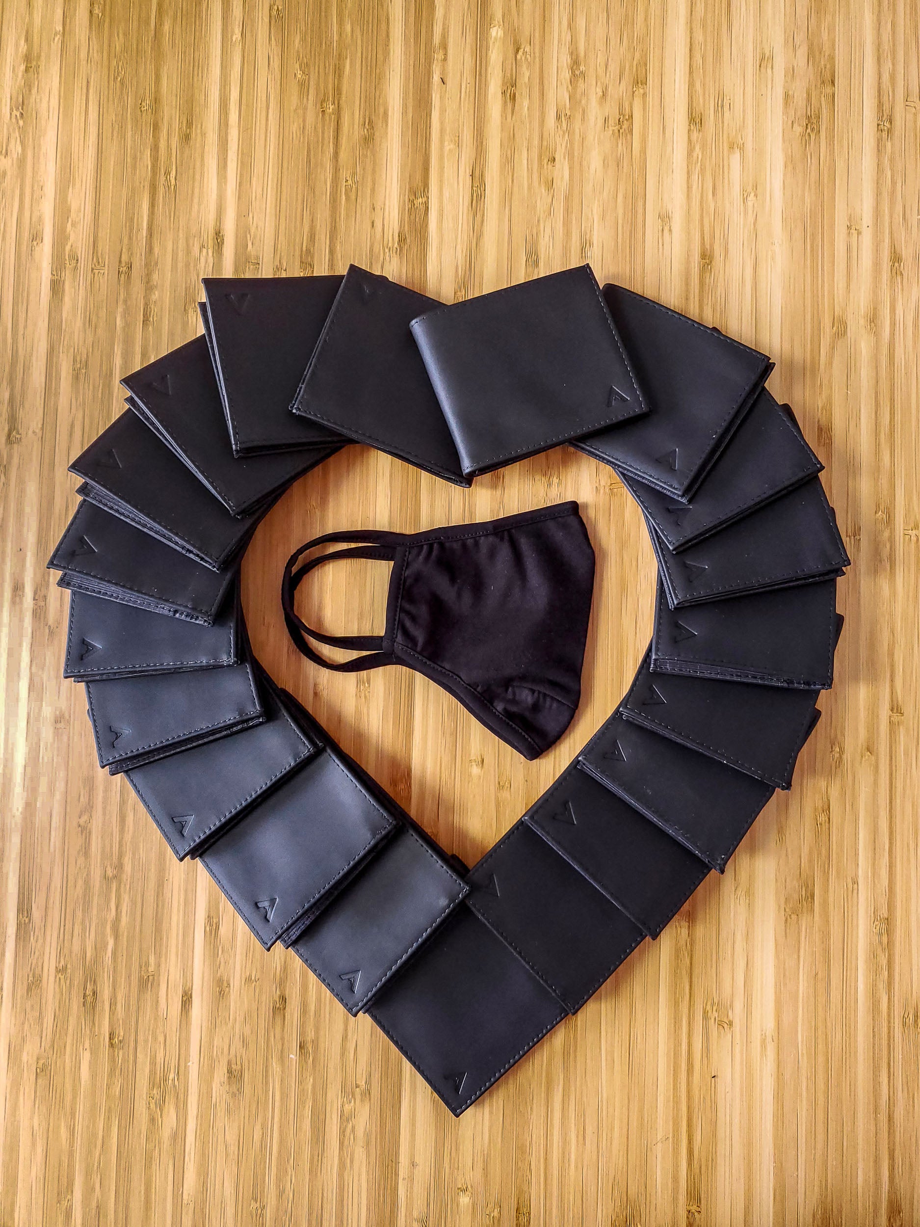 Black face mask surrounded by a heart made up of black leather wallets.