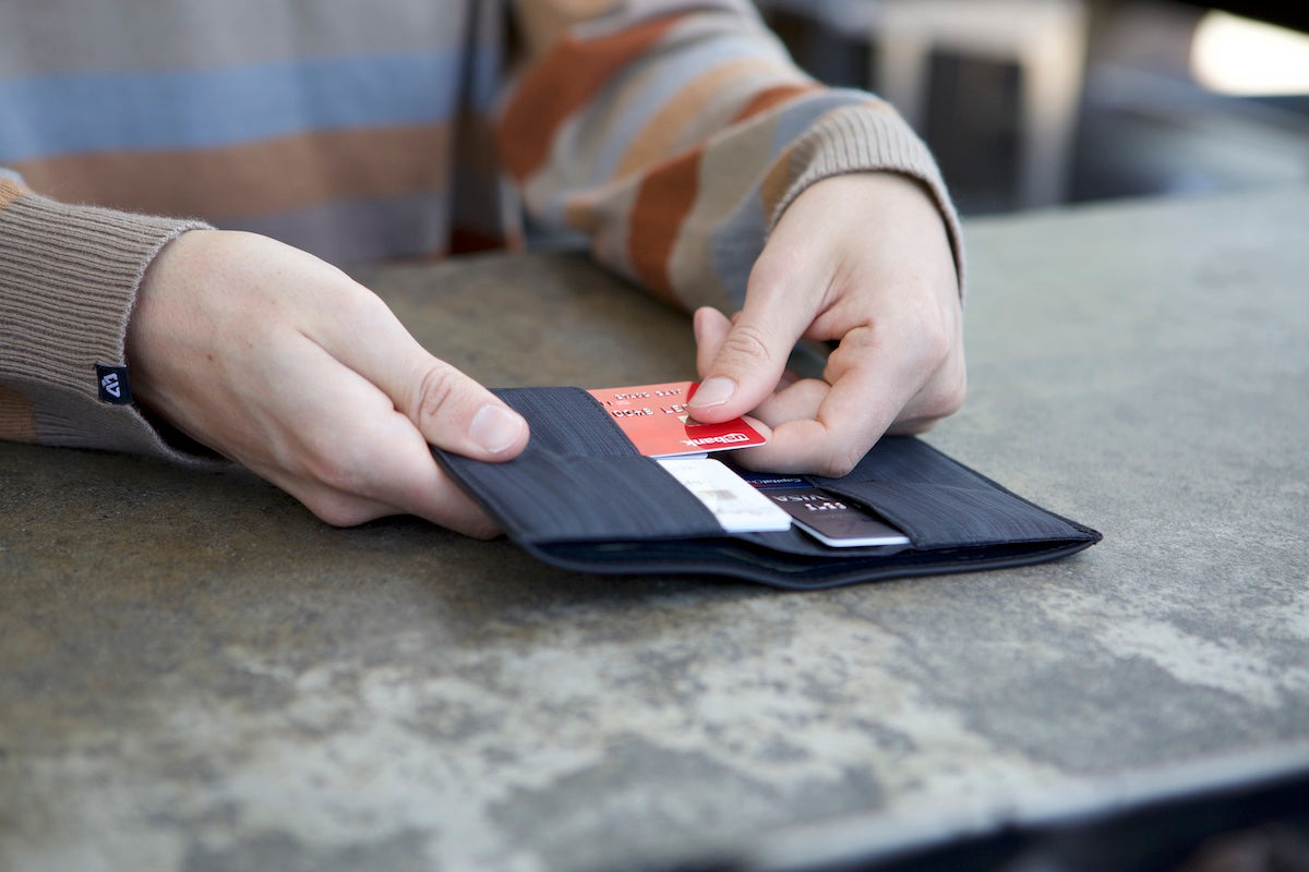 Person is taking a credit card out of a full, slim black wallet.