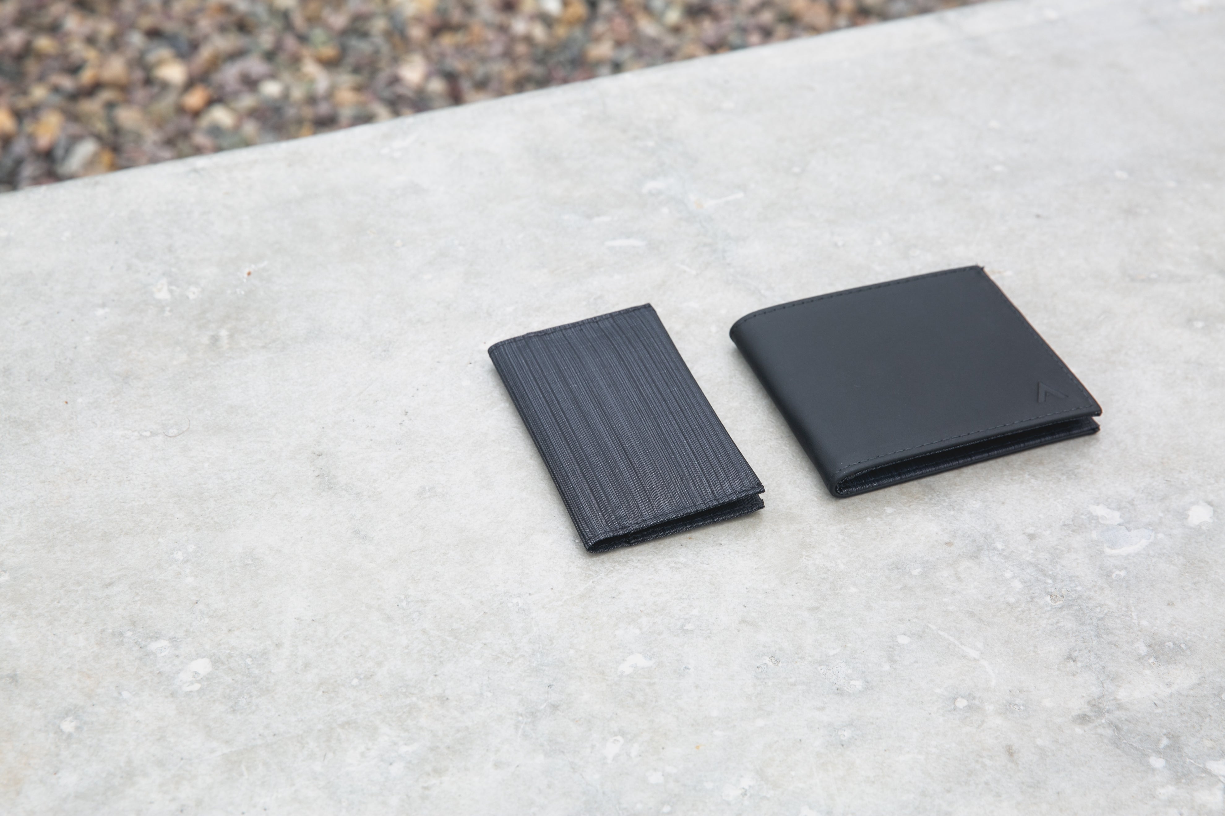 On the left is a thin nylon cardholder in an onyx black color, on the right is a traditional thin black leather wallet.