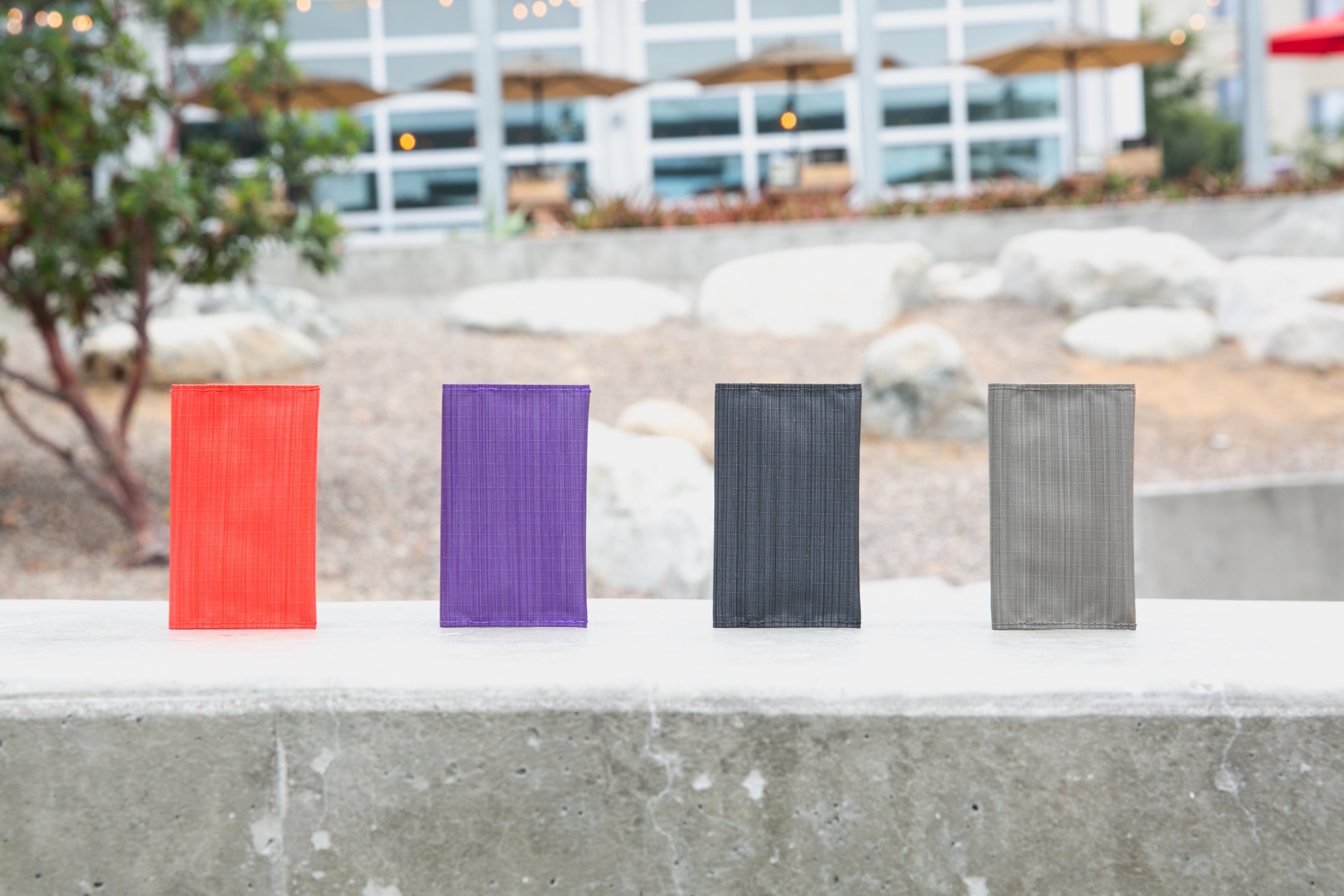 4 vibrant colors of vegan nylon wallets, an orange-red, purple, black, and gray in order from left to right.