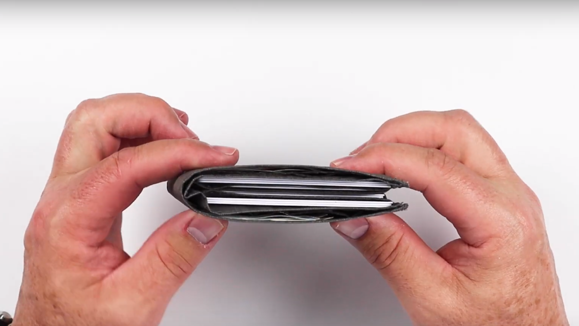 Picture of two hands holding a very thin wallet that is filled with nearly a dozen credit cards.