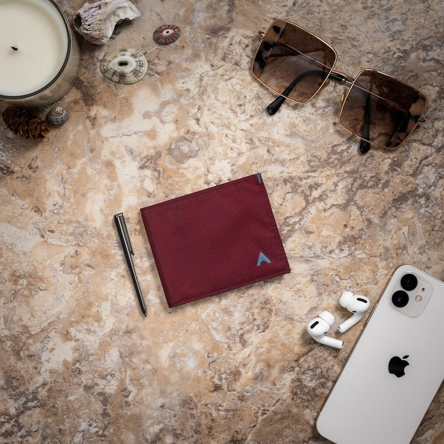 Allett mulberry RFID sports wallet and micropen on a table with other everyday carries, including sunglasses and a smartphone -Allett Sport Wallet RFID Nylon Front Pocket Wallet mulberry