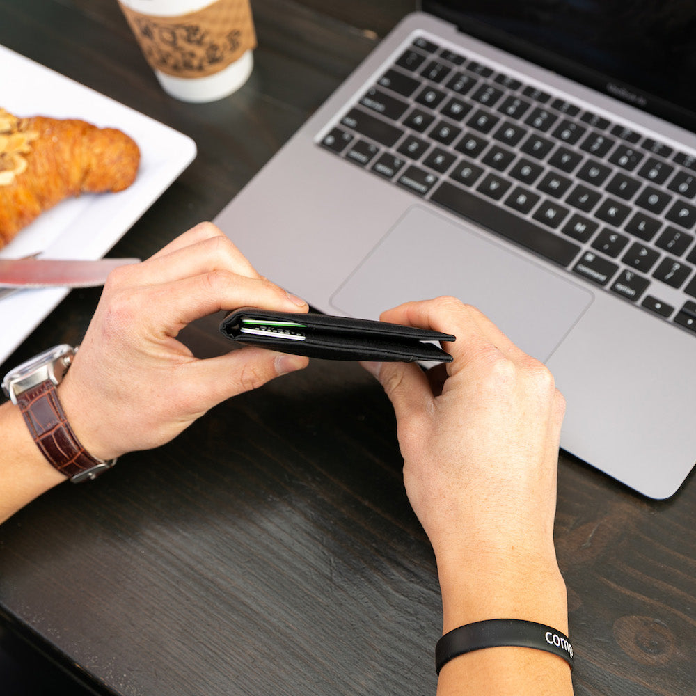 Individual gripping the onyx black leather coin wallet shut, illustrating its slender construction even when packed with cards, visible from the side of the wallet. allett leather coin wallet onyx-black